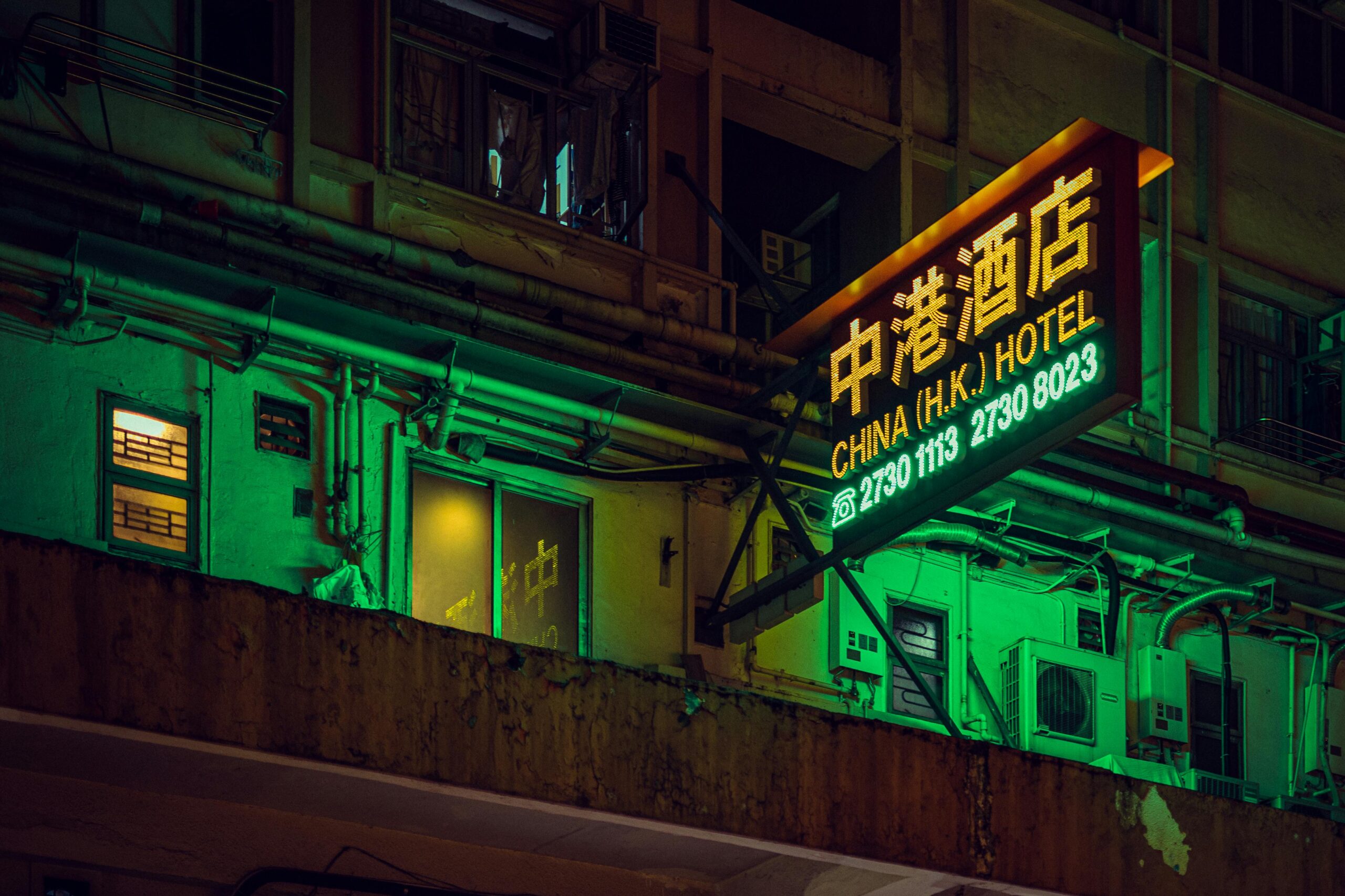 A neon-lit hotel sign illuminates the bustling streets of Hong Kong, capturing the city's vibrant nightlife.